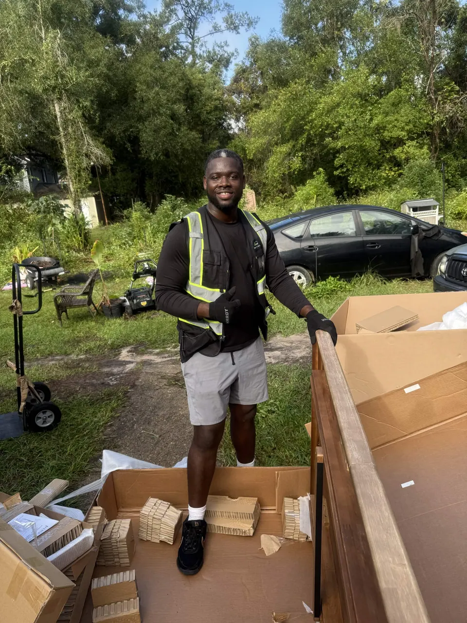 Delivery team member beside packaged furniture items outside a home.