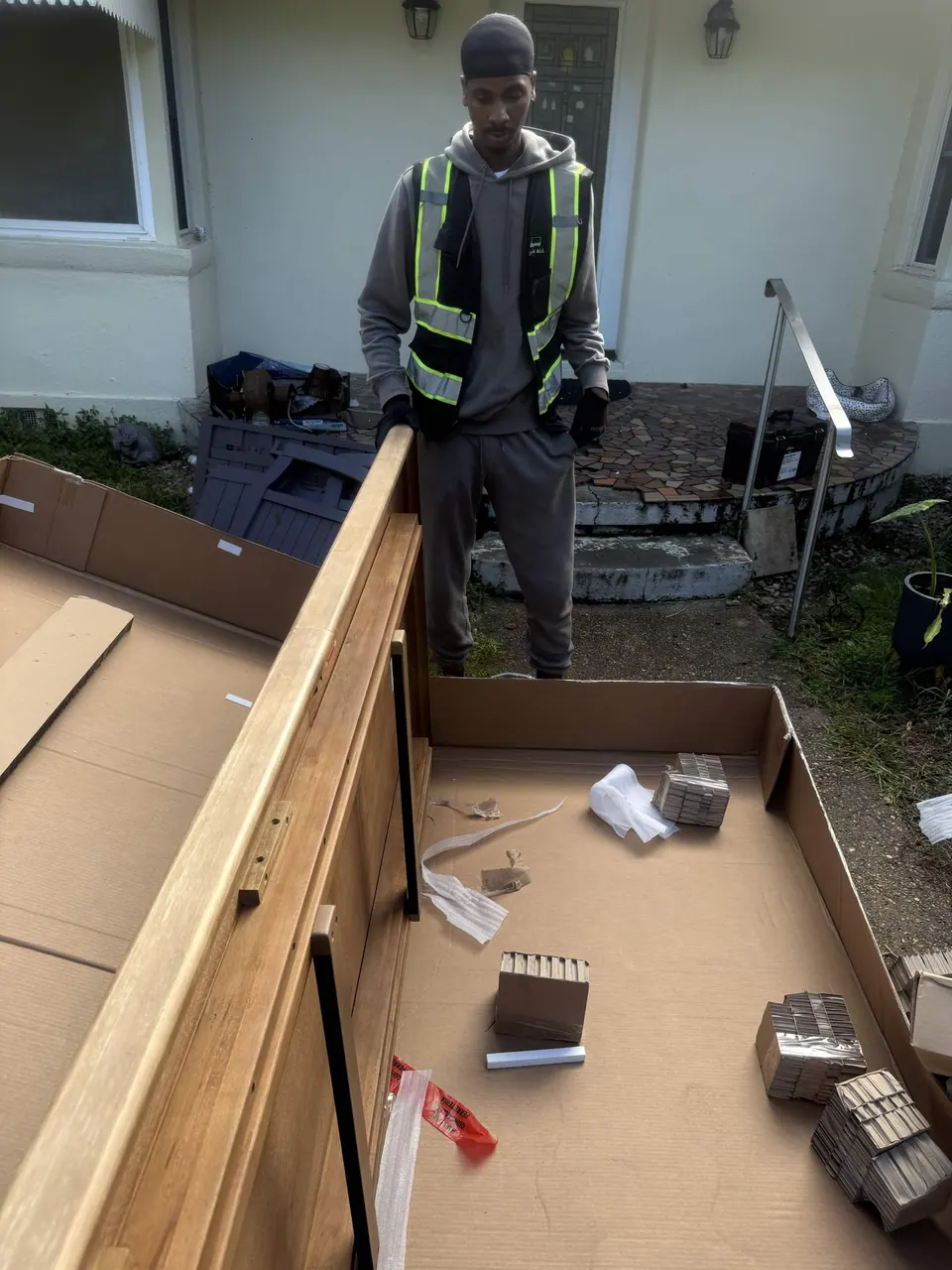 Delivery team member working with furniture and packaging outside a home.